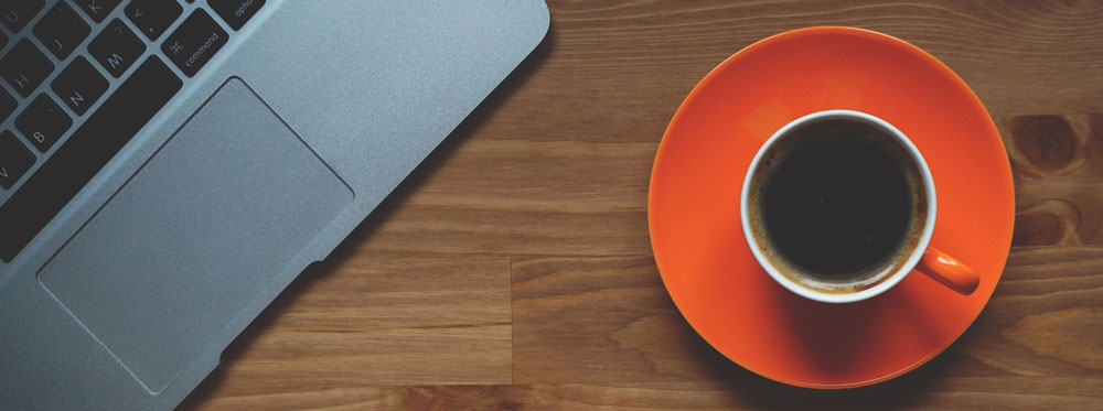 A cup of coffee on an orange saucer and part of a laptop used for business productivity tools and technology.