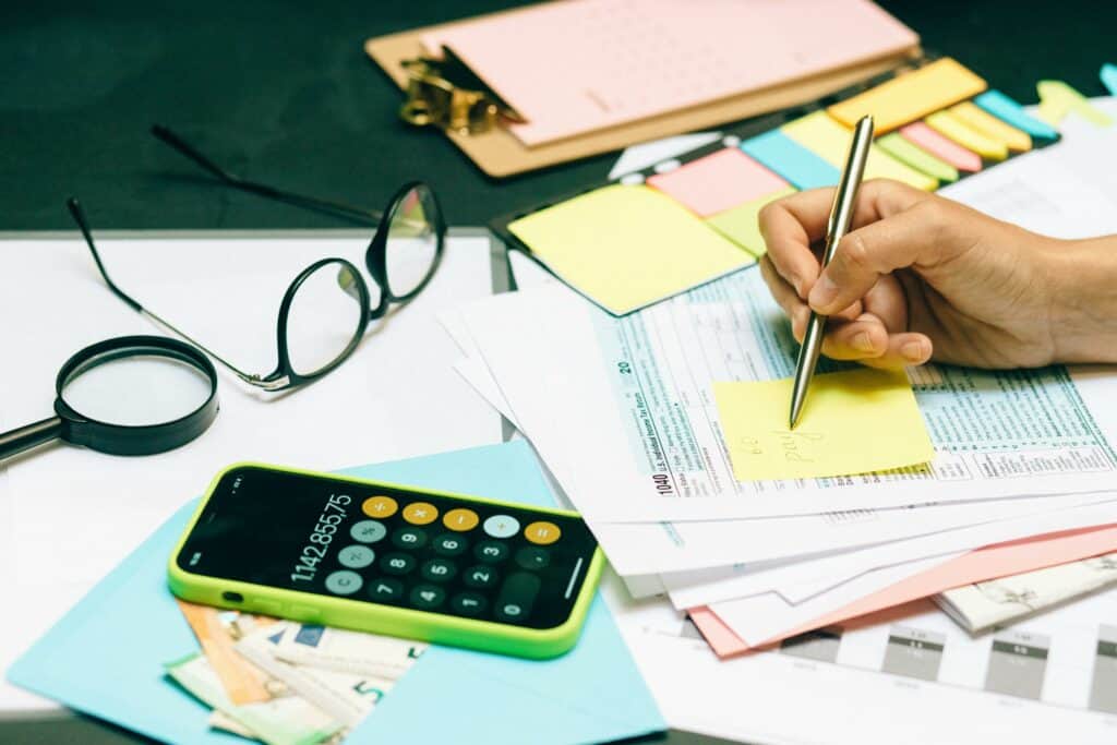 A persons hand writing on a stack of financial documents related to timely payments of loans