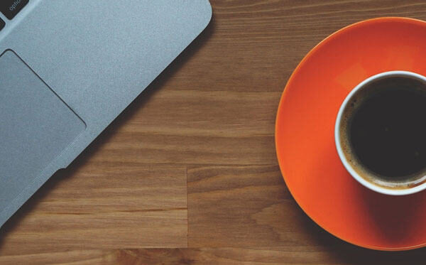 A cup of coffee on an orange saucer and part of a laptop used for business productivity tools and technology.