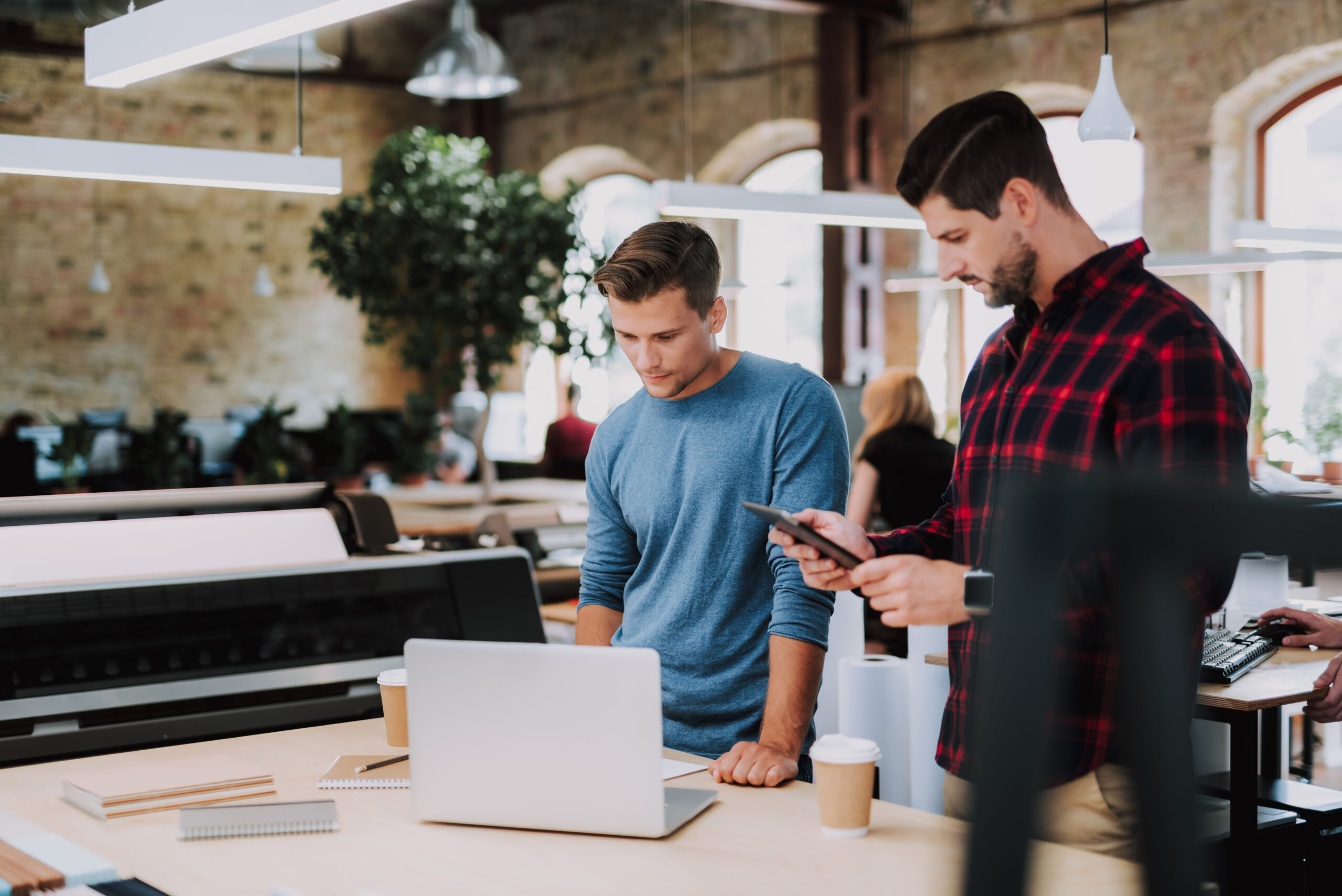 Serious smart young colleagues standing in the office while working together on design project