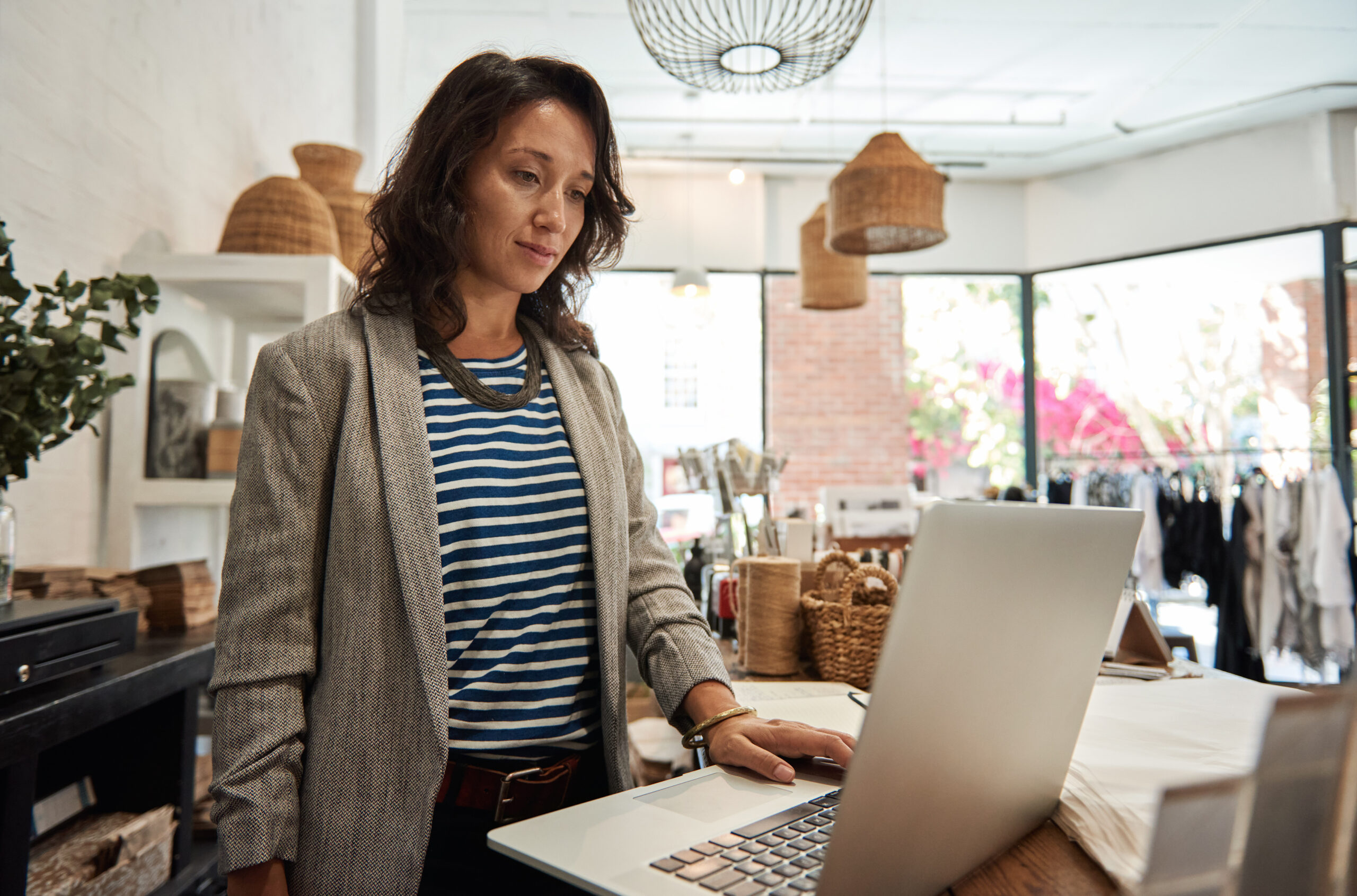 Small business owner working online with a laptop while standing behind a counter in her stylish boutique