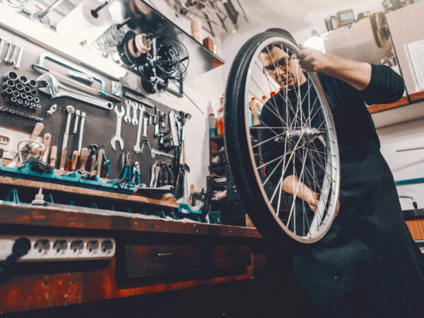 Man holding bicycle wheel in hands while standing in workshop.
