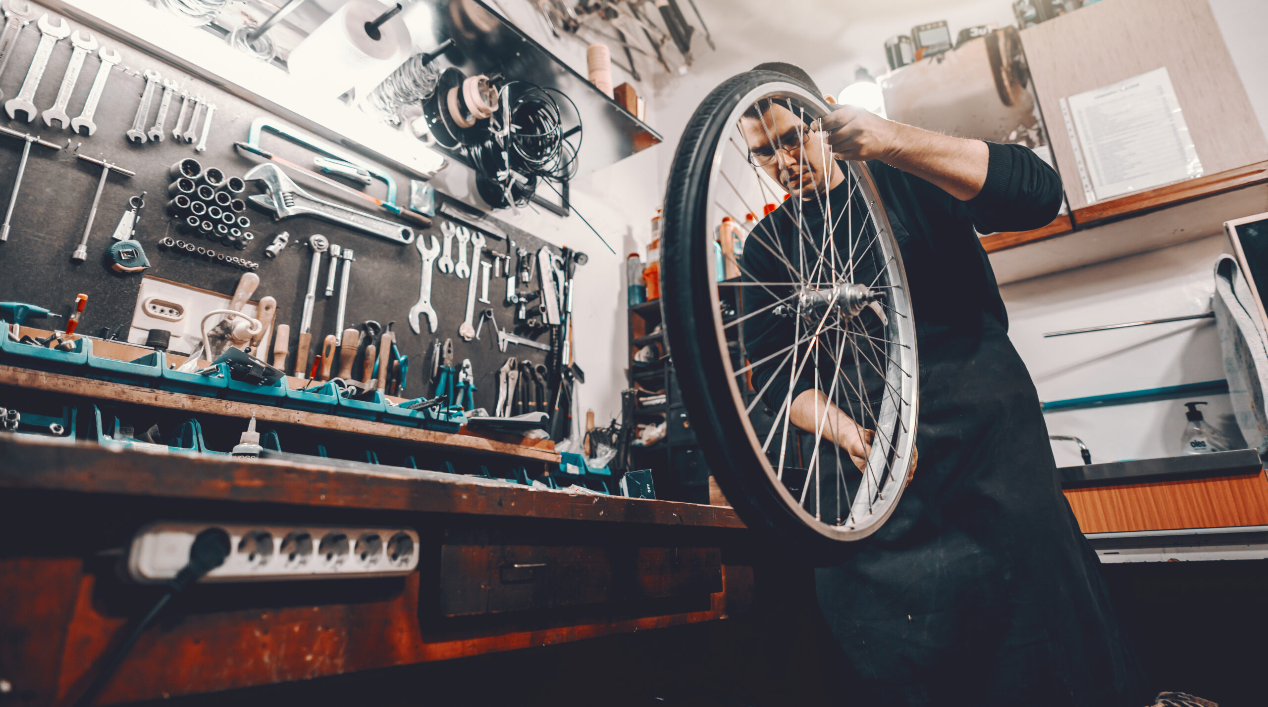 Man holding bicycle wheel in hands while standing in workshop.