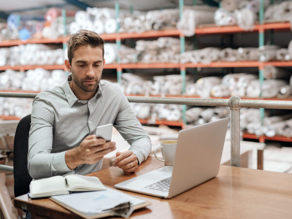 Warehouse manager checking his cellphone while working in his office
