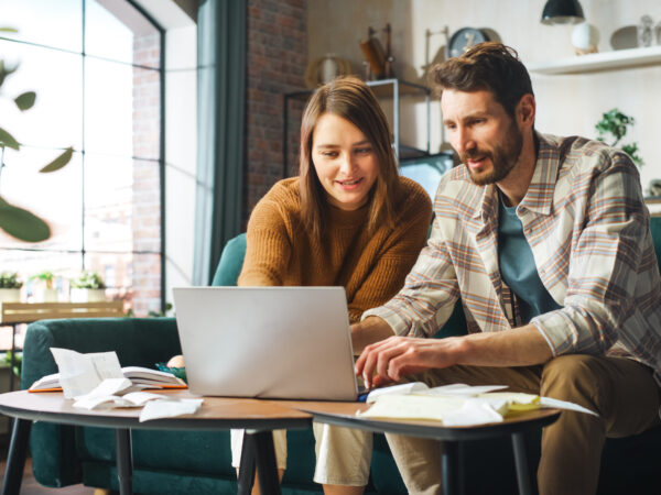 Doing Accounting at Home: Happy Couple Using Laptop Computer, Sitting on Sofa in office.